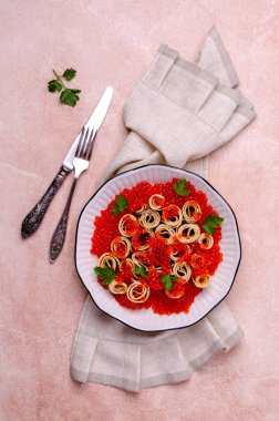 Hafif çimento arka planında kırmızı balık yumurtası ve seramik tabakta kızarmış krep. Seçici odak.