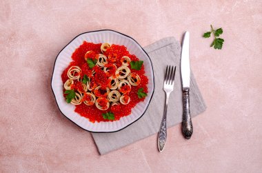 Hafif çimento arka planında kırmızı balık yumurtası ve seramik tabakta kızarmış krep. Seçici odak.