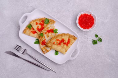 Hafif çimento arka planında kırmızı balık yumurtası ve seramik tabakta kızarmış krep. Seçici odak.