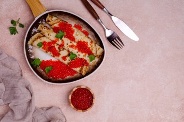 Hafif çimento arka planında kırmızı balık yumurtası ve seramik tabakta kızarmış krep. Seçici odak.