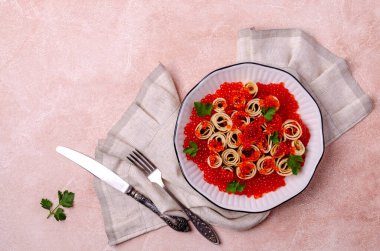 Hafif çimento arka planında kırmızı balık yumurtası ve seramik tabakta kızarmış krep. Seçici odak.