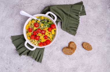 Hafif çimento arka planında seramik tabakta sebzeli ve yeşil soslu makarna. Seçici odak.