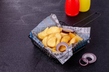 Siyah arka planda metal bir sepetin içinde kızarmış patates parçaları. Seçici odak.