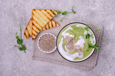 Beyaz soslu yeşil sebzeli kalın krema çorbası, gri arka planda chia tohumu ve bezelye filizi. Seçici odak.
