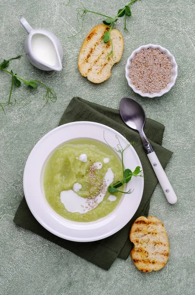 Thick cream soup of green vegetables with white sauce, chia seeds and pea sprouts on a green background. Selective focus.