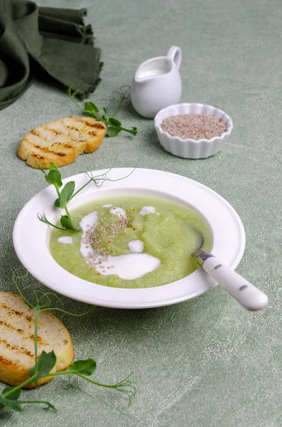 Thick cream soup of green vegetables with white sauce, chia seeds and pea sprouts on a green background. Selective focus.