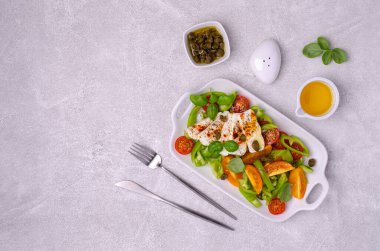 Taze sebze salatası. Sarı ve kırmızı domates, yeşil biber, kapari, fesleğen ve baharatlı peynir. Gri arka plan. Üst görünüm.