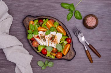 Taze sebze salatası. Sarı ve kırmızı domates, yeşil biber, kapari, fesleğen ve baharatlı peynir. Ahşap arka plan. Üst görünüm.