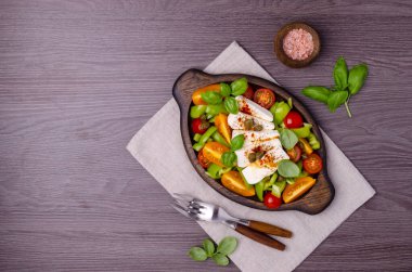 Taze sebze salatası. Sarı ve kırmızı domates, yeşil biber, kapari, fesleğen ve baharatlı peynir. Ahşap arka plan. Üst görünüm.