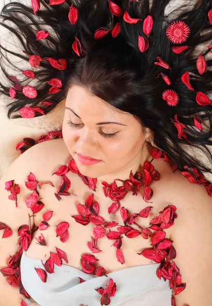 Overweight woman relaxing with petals in hair — Stock Photo, Image