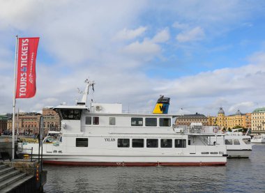 Stockholm, İsveç-18 Eylül 2025: Kimliği belirsiz kişiler Stromkajen Limanı 'nda demirlemiş tekneler ve tarihi binalar üzerinde yürüyor