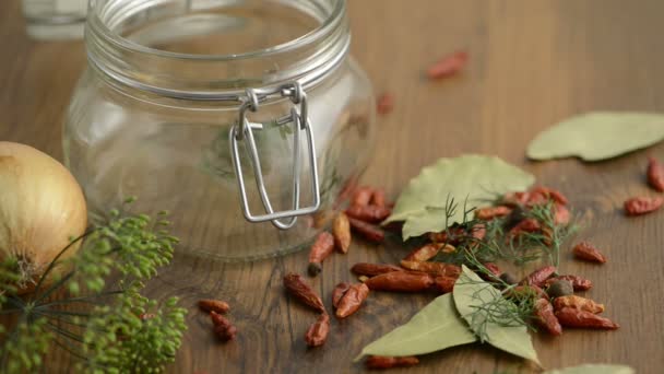 Épices comme l'aneth, le chili, les graines de moutarde tombant dans un pot de conserve sur une table. autour de la pose aussi des feuilles de laurier et un oignon . — Video