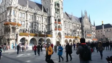 Münih'te Marienplatz'da yürüyen insanlar. Arka planda belediye binasında. Belediye binasının tepesine kadar kamera tavası.