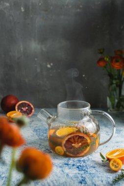 Turunçgil kanı, portakallı çay ve turuncu çiçekli açık mavi masadaki buhar.