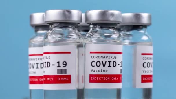 Glazen injectieflacons met het covid-19 vaccin tegen blauwe achtergrond — Stockvideo