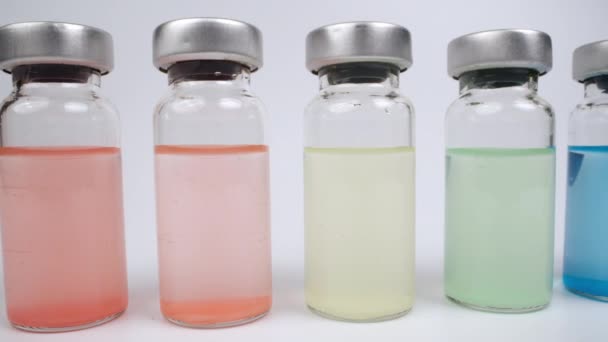 Glasflaschen mit verschieden farbigen Flüssigkeiten vor weißem Hintergrund — Stockvideo