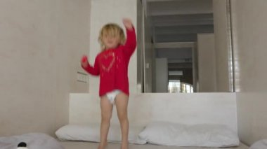 Küçük kız yatakta zıplıyor.