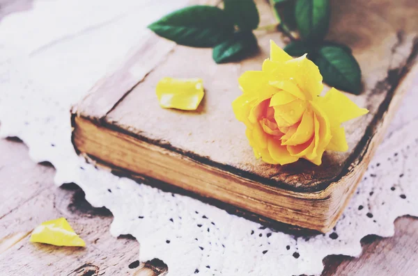 Yellow rose laying upon vintage book on lace doily — Stock Photo, Image