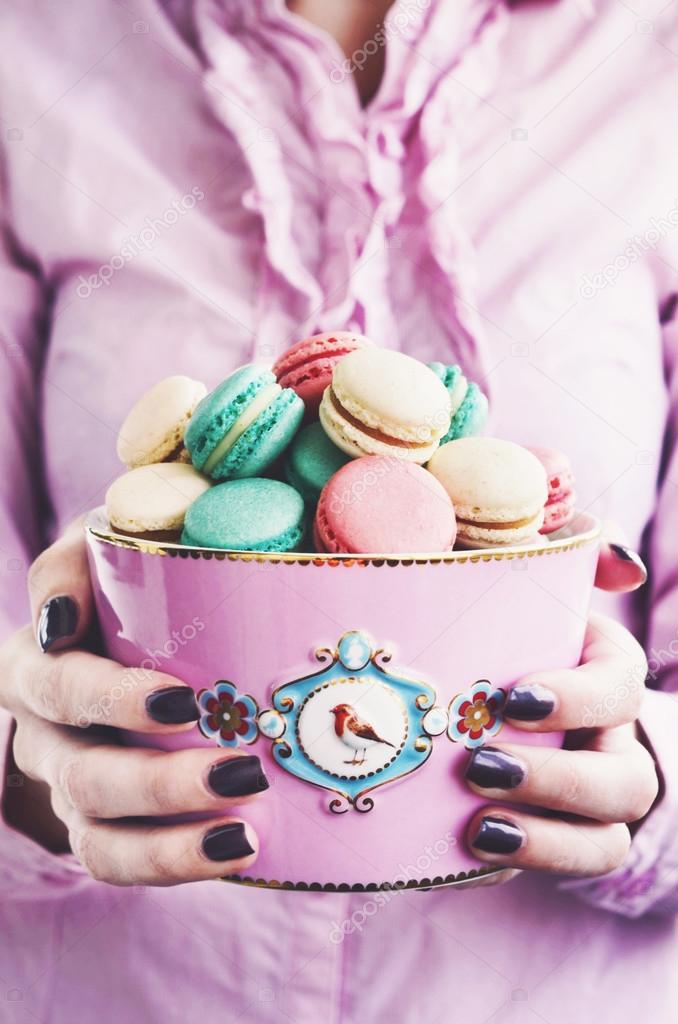 Girl holding pink bowl full of various macaroons - strawberry, vanilla and mint