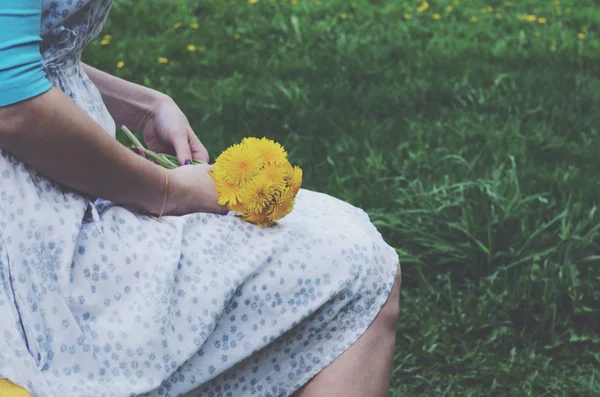Vintage elbiseli sarı dandelions demet tutan oturan kız — Stok fotoğraf