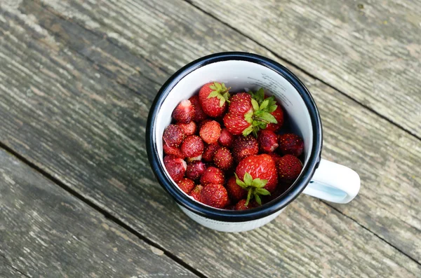 Wild strawberry in enamel cup on wooden table — Stock Photo, Image