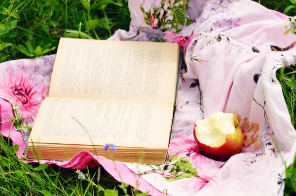 Maçã e livro aberto em grama verde — Fotografia de Stock