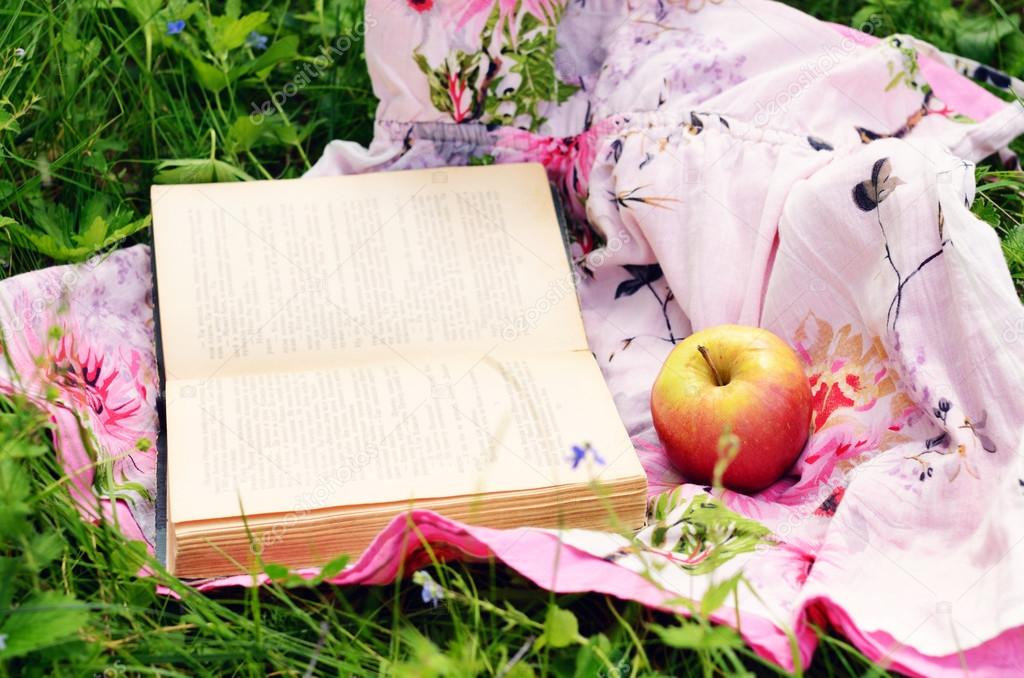 Apple and open book in green grass