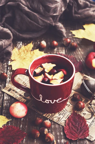 Apple and cranberry tea in red cup, warming scarf, apples, nuts — Stock Photo, Image