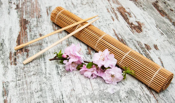 Ветка сакуры и палочки на бамбуковом коврике — стоковое фото