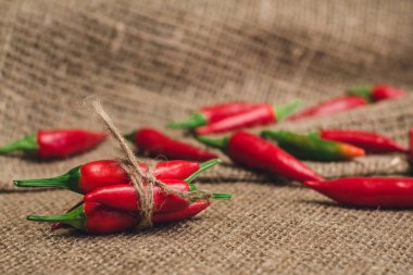 Keten peçeteye jüt iplikle bağlanmış küçük kırmızı biberler, seçici odak noktası.