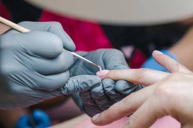 Gri eldivenli manikürcü tırnaklarını pembe jölelerle kaplıyor.