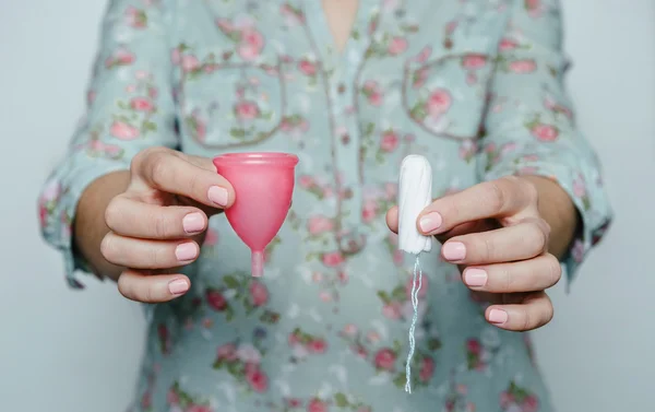 Mãos de mulher comparando copo menstrual com um tampão — Fotografia de Stock