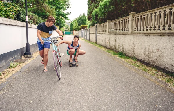 Двое мужчин весело катаются на велосипеде и скейтборде — стоковое фото