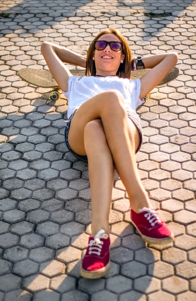 Young girl with a skateboard lying on the street in summer — Stock Photo, Image