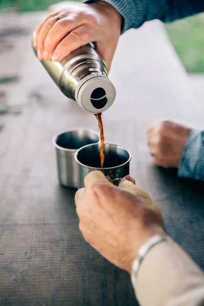Sénior casal mãos derramando café de garrafa térmica — Fotografia de Stock