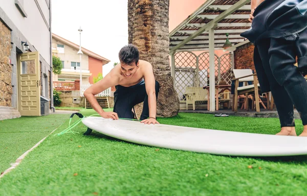 Surfer man with wetsuit waxing woman surfboard — Stock Photo, Image