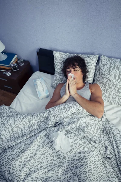 Sick man sneezing and covering nose with tissue — Stock Photo, Image