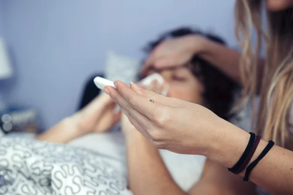 Женщина смотрит температура больного мужчины в термометре — стоковое фото