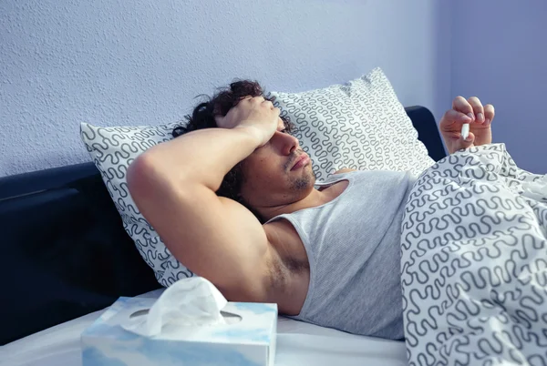 Άρρωστος άνθρωπος ψάχνει θερμοκρασίας στο θερμόμετρο στο κρεβάτι — Φωτογραφία Αρχείου