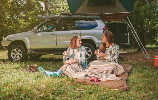 Women friends resting under blanket in campsite