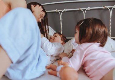 Rahatlamış anne ve oğullar yatağın üzerinde oynuyorlar.