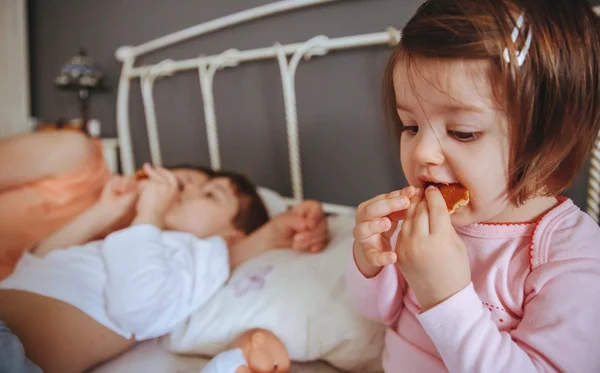 Расслабленная маленькая девочка ест печенье над кроватью — стоковое фото