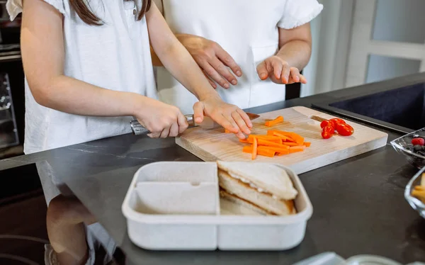 Onherkenbare moeder die haar dochter leert groenten te snijden voor de lunch. — Stockfoto