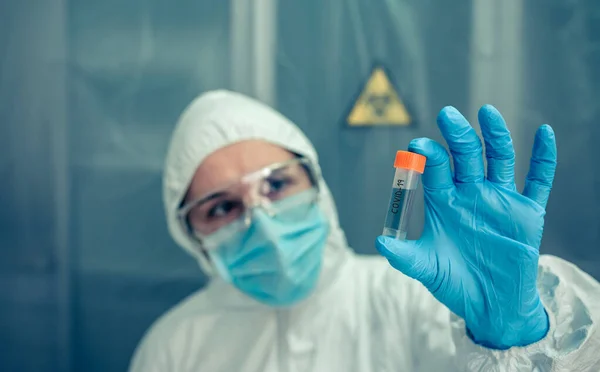 Cientista com terno de proteção olhando frasco no laboratório — Fotografia de Stock