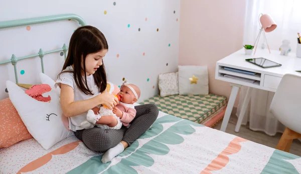 Bambina che gioca con la sua bambola e lascia il tablet sulla scrivania — Foto Stock