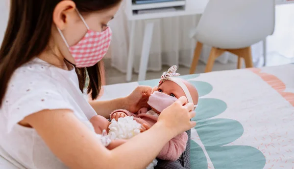 Mädchen mit Maske setzt kleine Maske auf ihre Puppe — Stockfoto