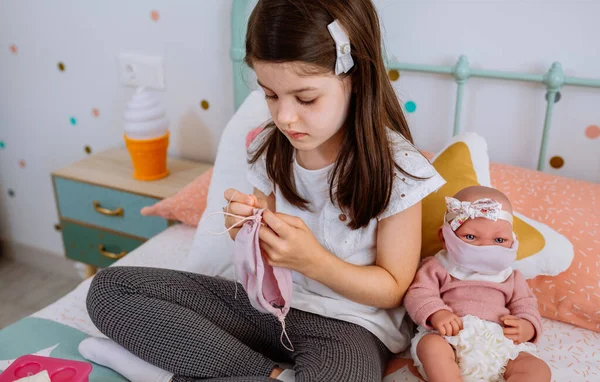 Mädchen näht Gesichtsmasken für sich und ihre Babypuppe — Stockfoto