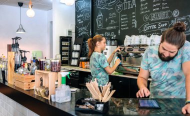 İş arkadaşı tableti kullanırken garson kahve makinesi hazırlıyor.