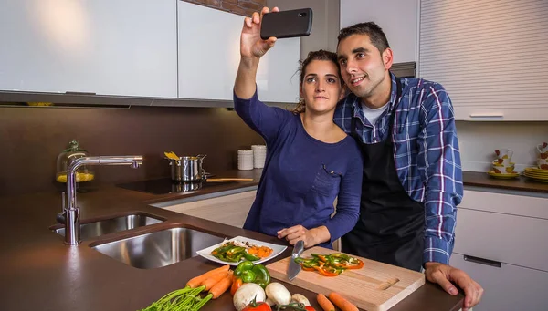 Пара в кухне приготовления пищи и делать селфи со смартфоном — стоковое фото