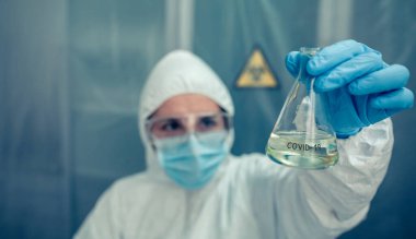 Koruyucu kıyafetli bir bilim adamı laboratuarda test tüpü arıyor.